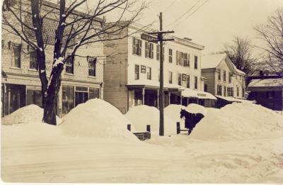 Black and white image of a horse standing on a street lined in mounds of snow